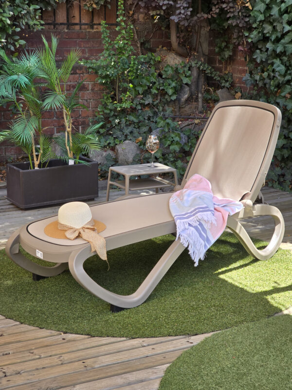 reposera para piscina omega de nardi Italia color taupe sobre un deck frente a un Jardin verde