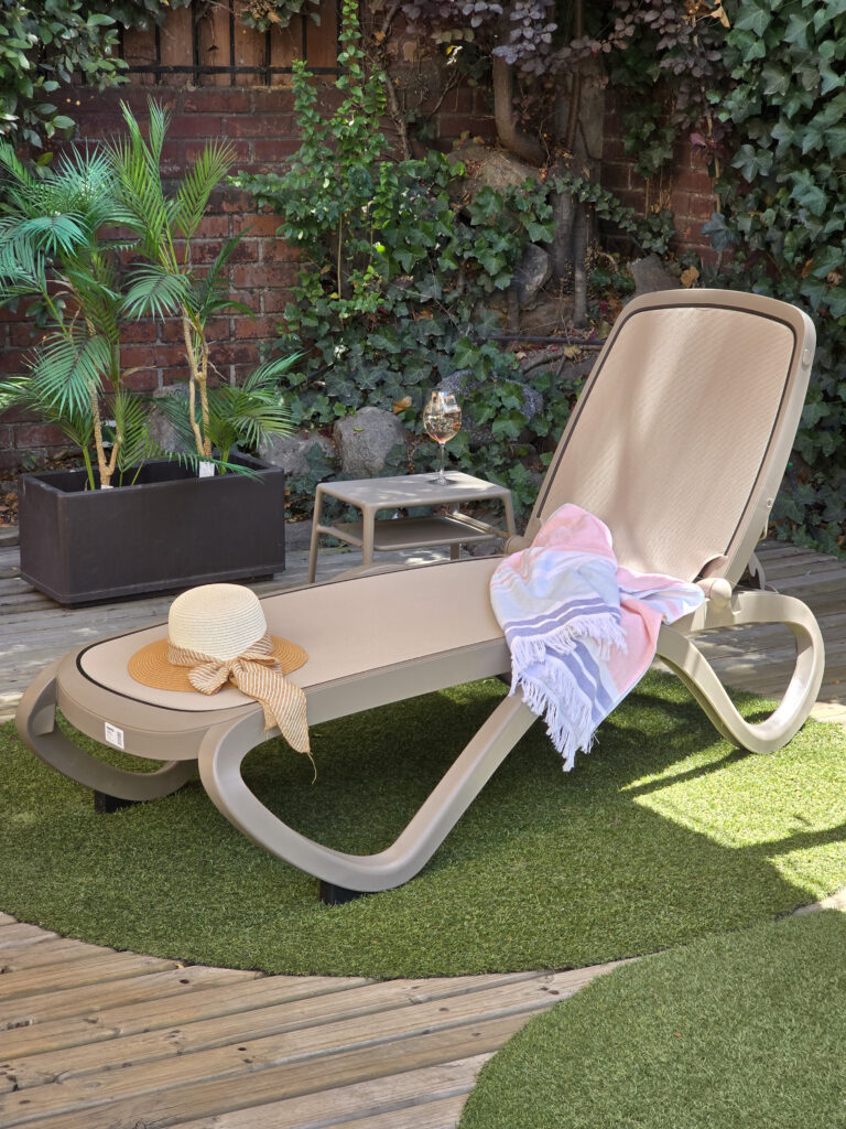 reposera para piscina omega de nardi Italia color taupe sobre un deck frente a un Jardin verde